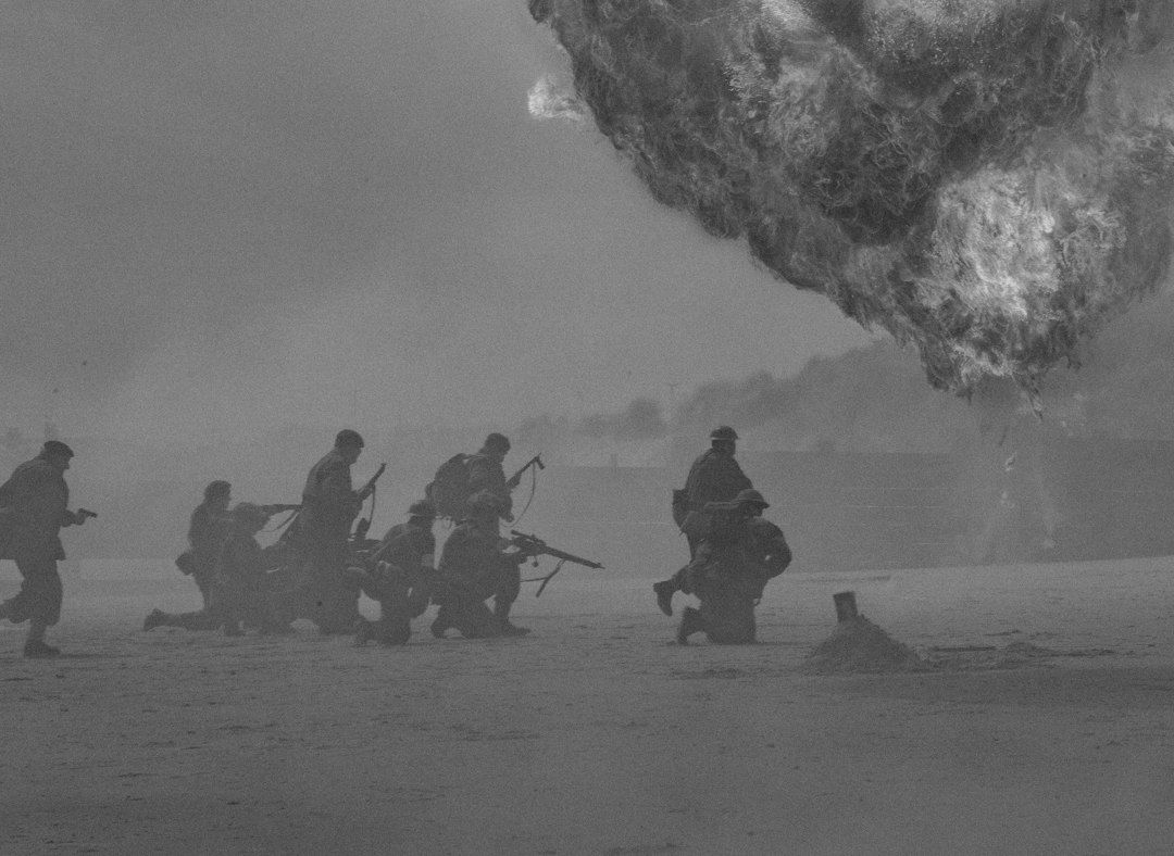 Grayscale film scene of soldiers advancing through smoke beneath a looming cloud