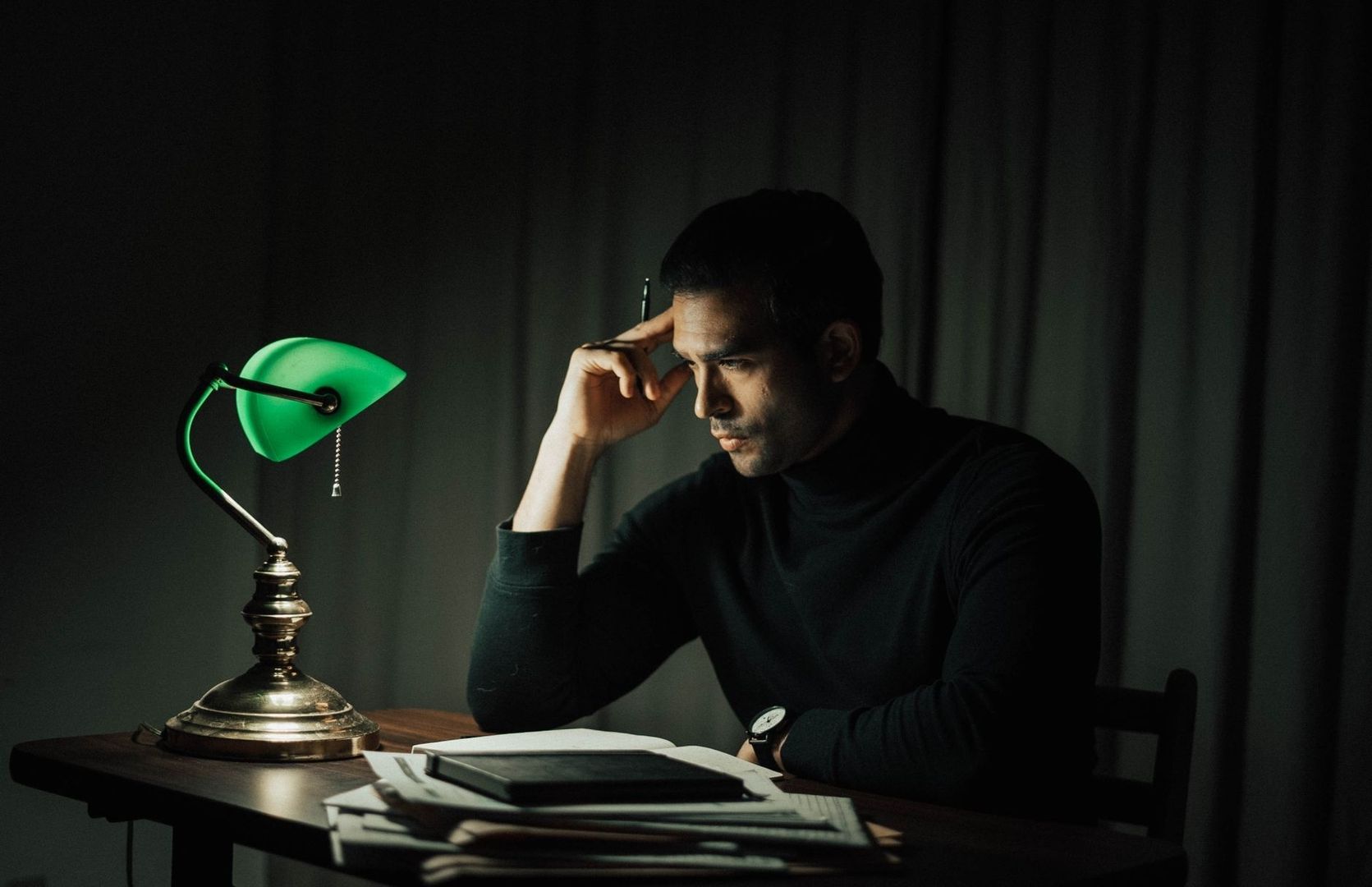 Man sits pensively beside a glowing green vintage desk lamp