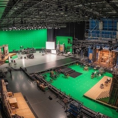 Large film studio with green screens, lighting rigs, and set pieces